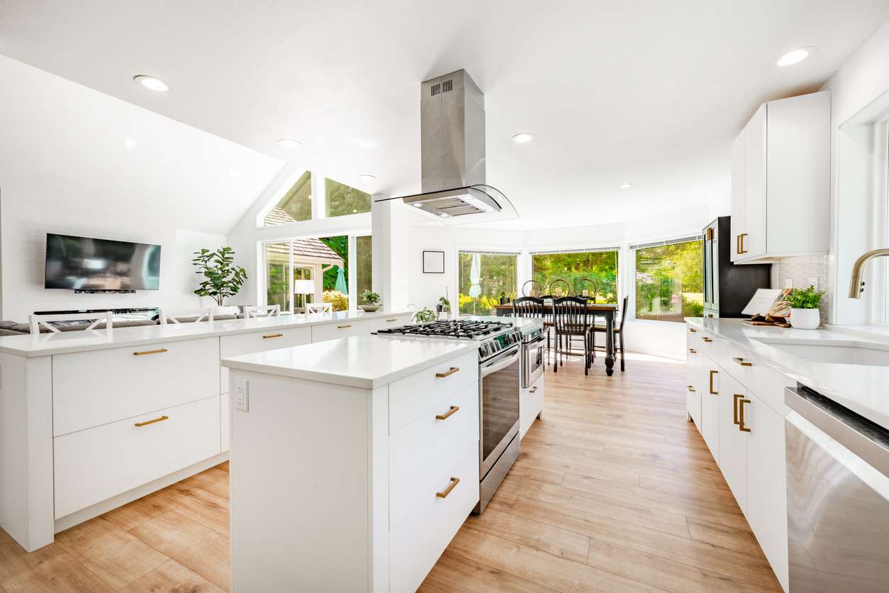 Open-concept kitchen remodel in Boise with white cabinets, quartz countertops, island range hood, and hardwood floors overlooking backyard